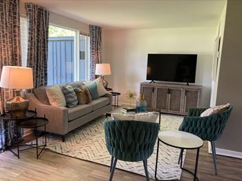 A living room with a grey couch, a green chair, a small table, and a television at Townhomes at 28th, Columbus, IN, 47201